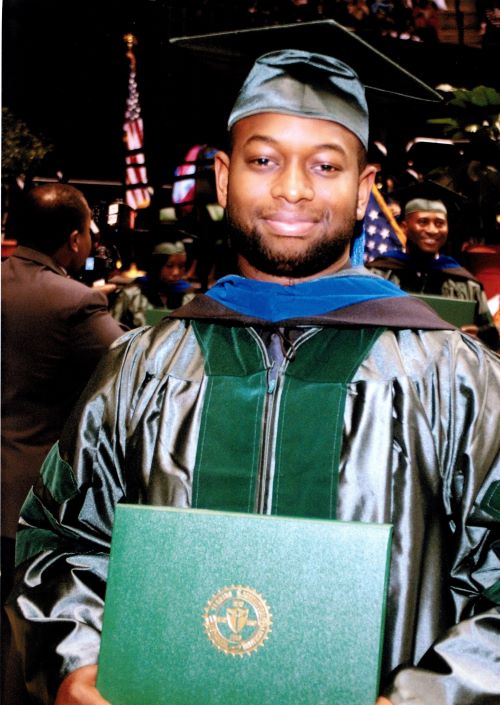 Dr. Brooks in a graduation cap and gown, holding his degree.
